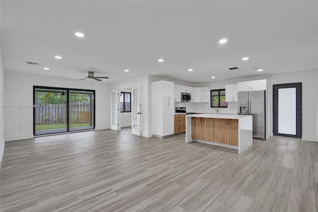 kitchen with light hardwood / wood-style flooring, appliances with stainless steel finishes, white cabinetry, a spacious island, and a healthy amount of sunlight