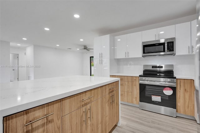 kitchen featuring white cabinets, ceiling fan, stainless steel appliances, light stone countertops, and light hardwood / wood-style flooring