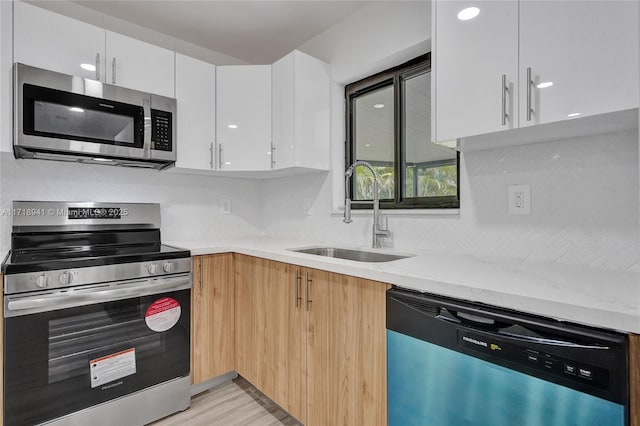 kitchen with appliances with stainless steel finishes, white cabinetry, sink, decorative backsplash, and light stone countertops