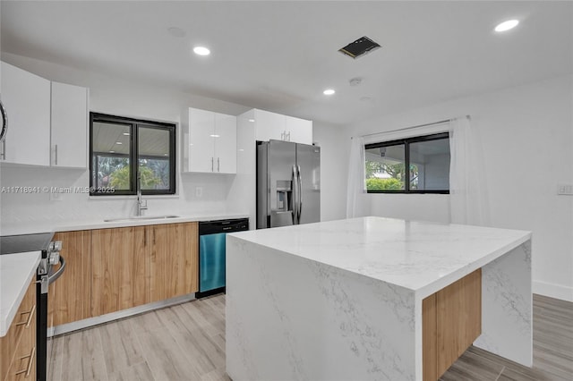 kitchen featuring stainless steel appliances, white cabinetry, a center island, and sink