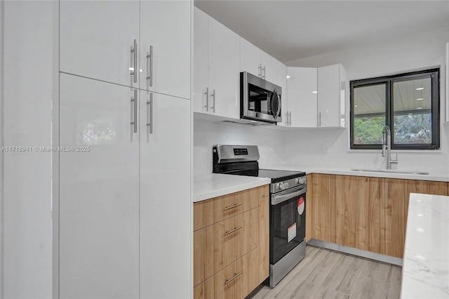 kitchen featuring sink, light hardwood / wood-style flooring, stainless steel appliances, tasteful backsplash, and white cabinets