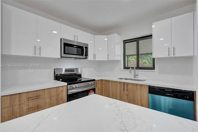 kitchen featuring sink, white cabinetry, stainless steel appliances, light stone counters, and decorative backsplash