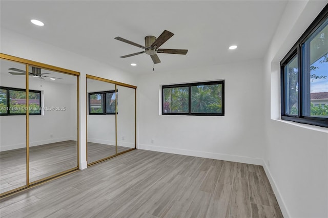 unfurnished bedroom with ceiling fan, light hardwood / wood-style flooring, and multiple closets