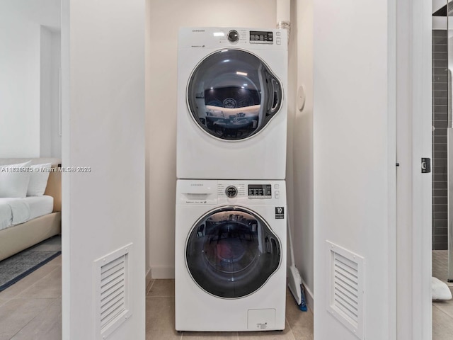 clothes washing area with light tile patterned floors and stacked washer and dryer