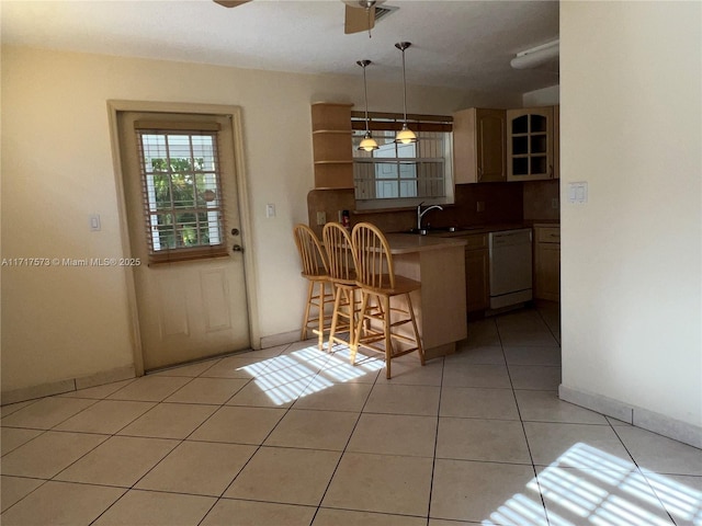 kitchen featuring kitchen peninsula, light tile patterned floors, dishwasher, hanging light fixtures, and a breakfast bar area