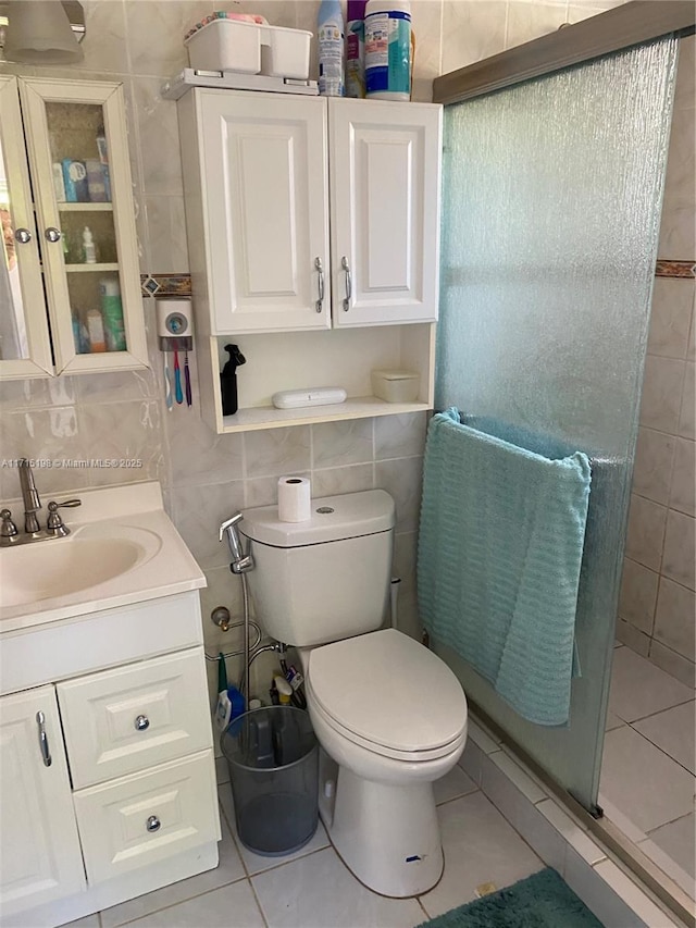 bathroom with vanity, a shower with door, tile patterned flooring, toilet, and tile walls