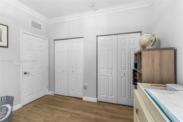 bedroom featuring multiple closets, crown molding, and hardwood / wood-style flooring