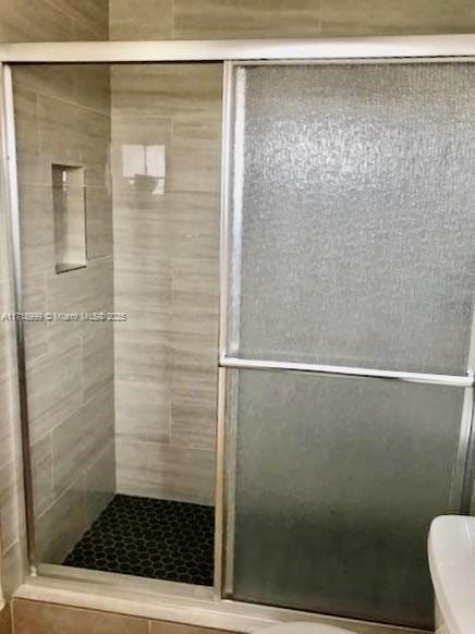 bathroom featuring a shower with door and toilet