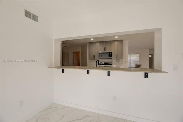 kitchen with kitchen peninsula, a breakfast bar area, gray cabinets, decorative backsplash, and appliances with stainless steel finishes