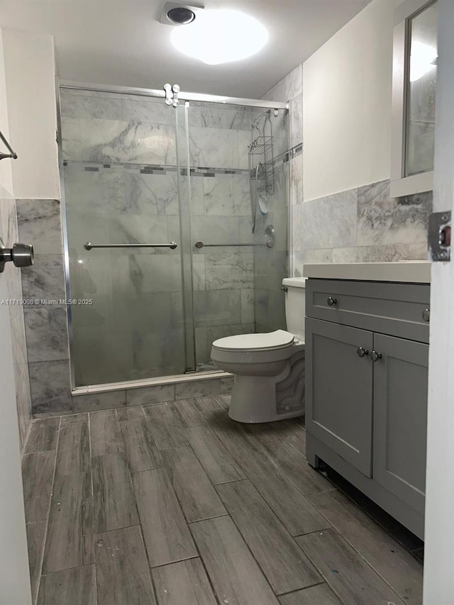 bathroom with vanity, an enclosed shower, tile walls, and toilet