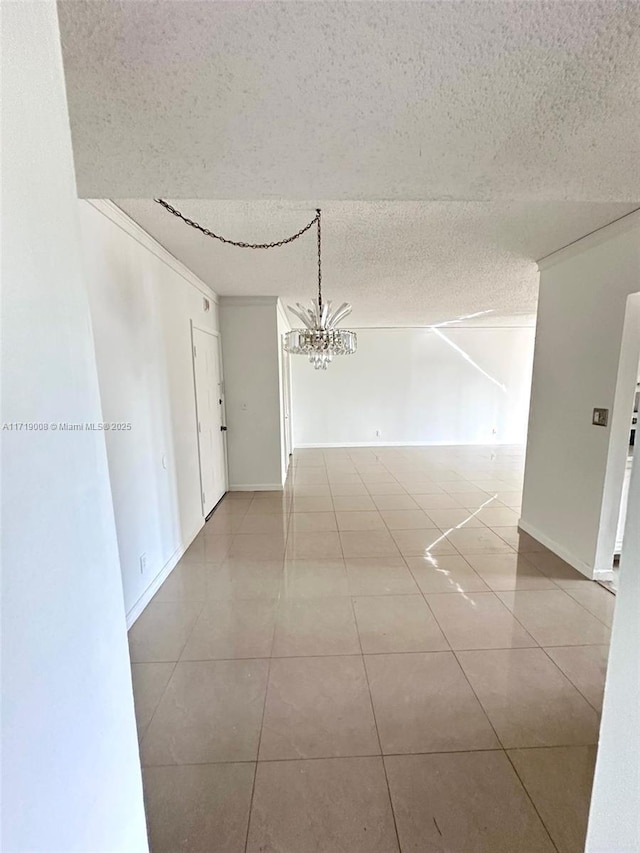 empty room featuring a chandelier, a textured ceiling, ornamental molding, and tile patterned flooring