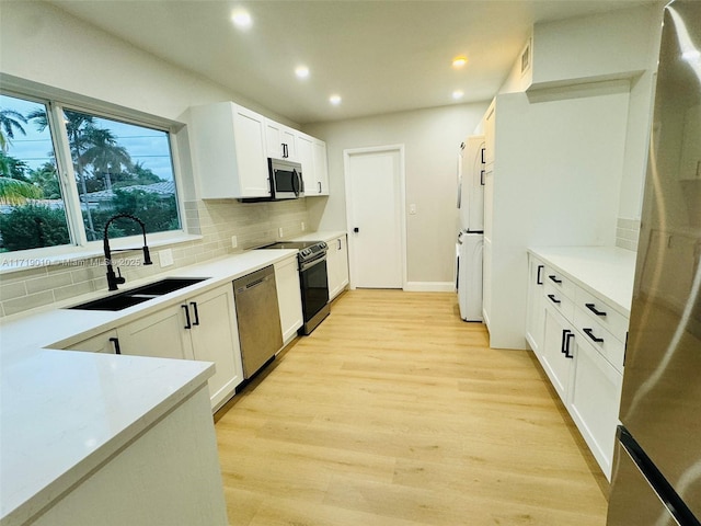 kitchen featuring white cabinets, sink, light hardwood / wood-style flooring, decorative backsplash, and appliances with stainless steel finishes