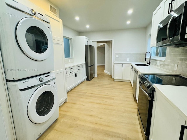 laundry area with stacked washing maching and dryer, sink, and light hardwood / wood-style flooring