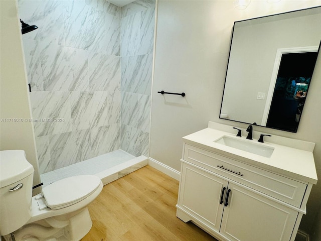 bathroom featuring a tile shower, vanity, wood-type flooring, and toilet