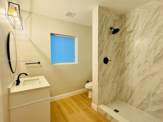 bathroom with hardwood / wood-style floors, vanity, a tile shower, and toilet