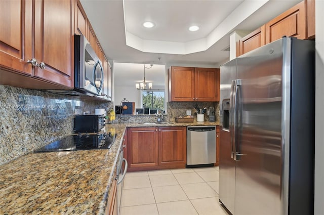 kitchen with sink, decorative light fixtures, a tray ceiling, light stone countertops, and stainless steel appliances