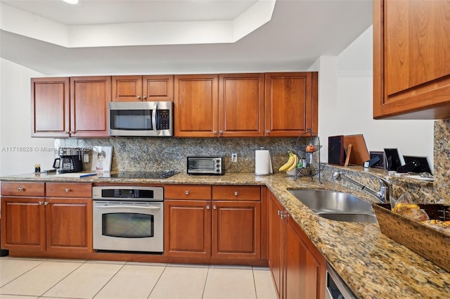 kitchen featuring light stone countertops, appliances with stainless steel finishes, a tray ceiling, sink, and light tile patterned floors