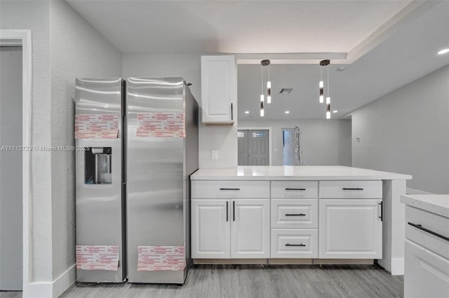 kitchen featuring kitchen peninsula, stainless steel fridge, pendant lighting, light hardwood / wood-style flooring, and white cabinetry