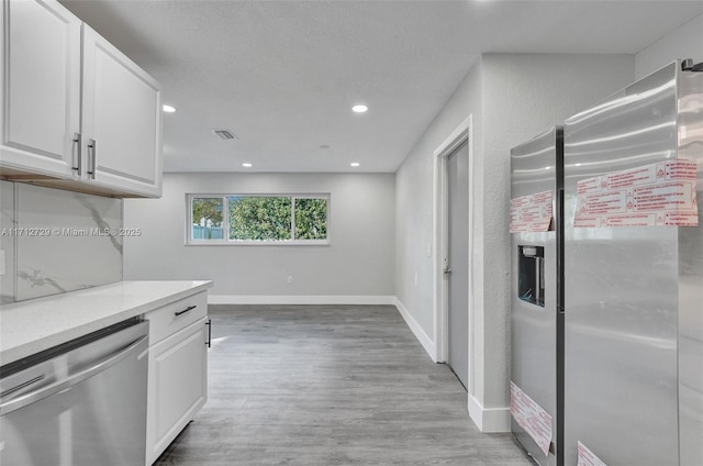 kitchen with light stone counters, light hardwood / wood-style flooring, white cabinets, and appliances with stainless steel finishes