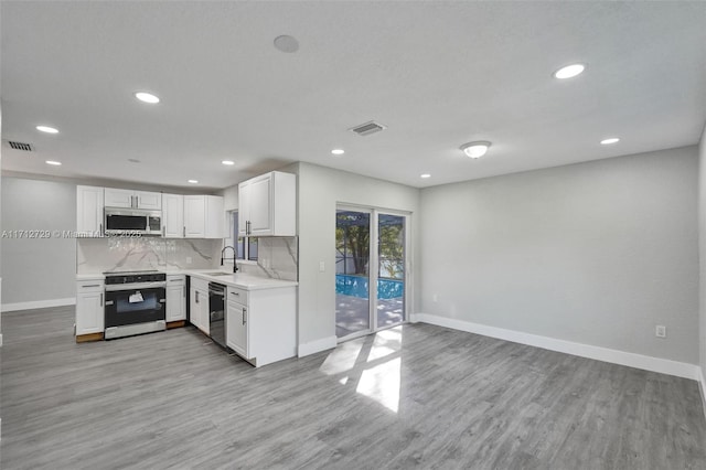 kitchen featuring sink, backsplash, light hardwood / wood-style floors, white cabinets, and appliances with stainless steel finishes