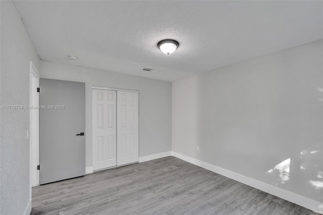 unfurnished bedroom featuring a textured ceiling, light hardwood / wood-style floors, and a closet