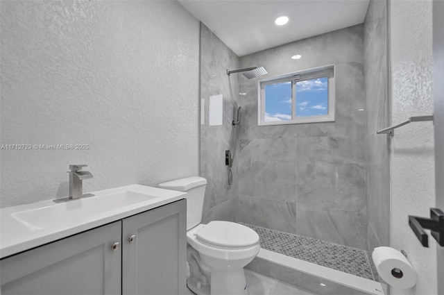 bathroom with tiled shower, vanity, and toilet