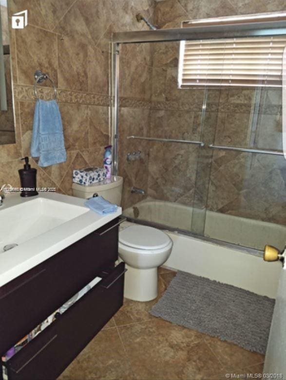 full bathroom featuring tile patterned floors, vanity, toilet, and bath / shower combo with glass door