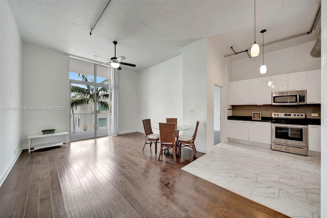 kitchen with white cabinetry, a towering ceiling, appliances with stainless steel finishes, and hanging light fixtures