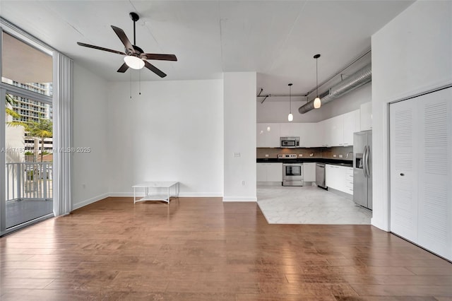 unfurnished living room featuring hardwood / wood-style floors, ceiling fan, and a high ceiling