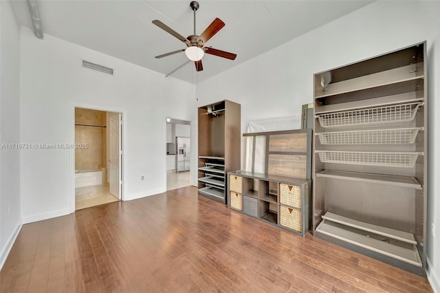 unfurnished bedroom with ensuite bathroom, refrigerator with ice dispenser, ceiling fan, hardwood / wood-style floors, and a high ceiling