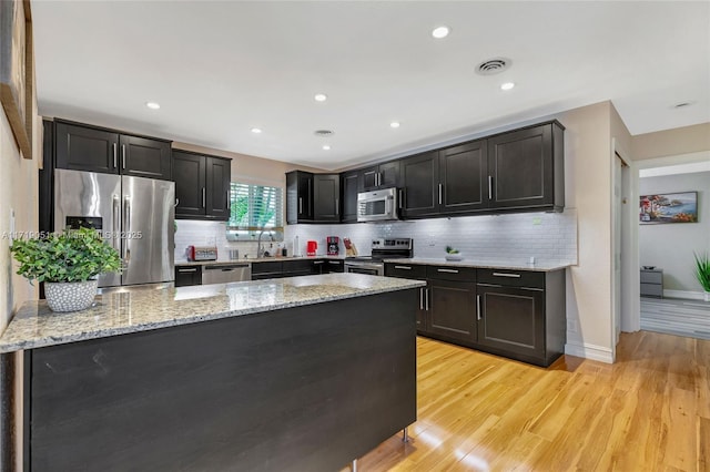 kitchen with light stone countertops, sink, light hardwood / wood-style flooring, decorative backsplash, and appliances with stainless steel finishes