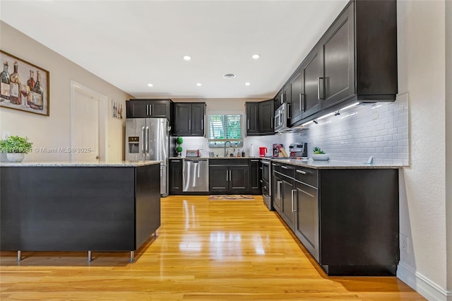 kitchen featuring backsplash, sink, light stone countertops, appliances with stainless steel finishes, and light hardwood / wood-style floors