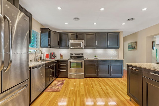 kitchen with light stone countertops, light wood-type flooring, and appliances with stainless steel finishes