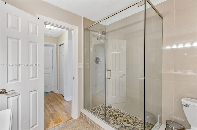 bathroom with hardwood / wood-style floors, toilet, and a shower with door