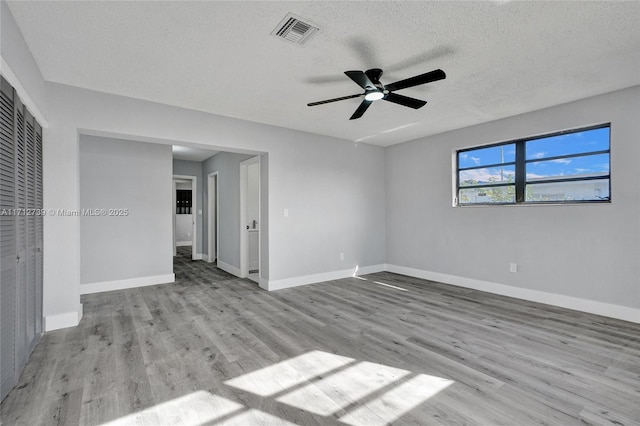 empty room with a textured ceiling, light wood-type flooring, and ceiling fan