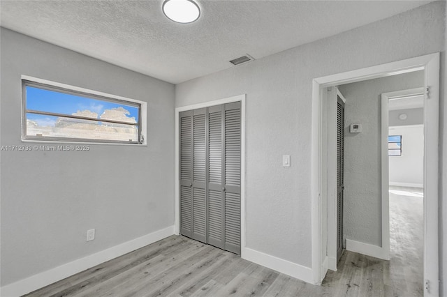 unfurnished bedroom featuring a closet, light hardwood / wood-style floors, and a textured ceiling