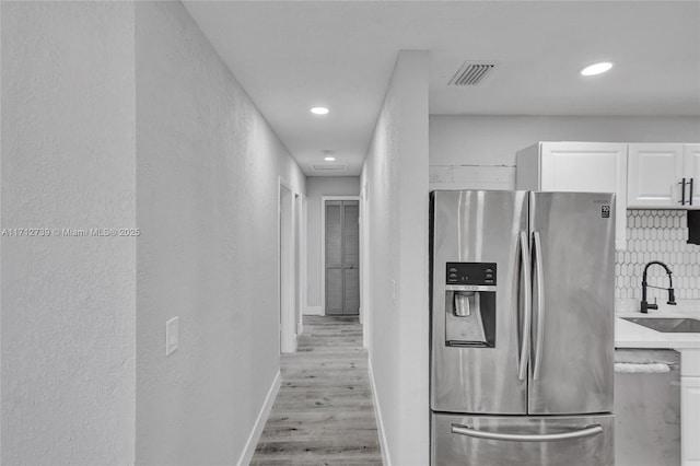 kitchen with backsplash, white cabinets, sink, light hardwood / wood-style floors, and stainless steel appliances