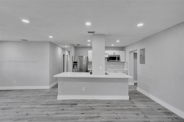 kitchen with backsplash, stainless steel appliances, white cabinets, a center island, and electric panel