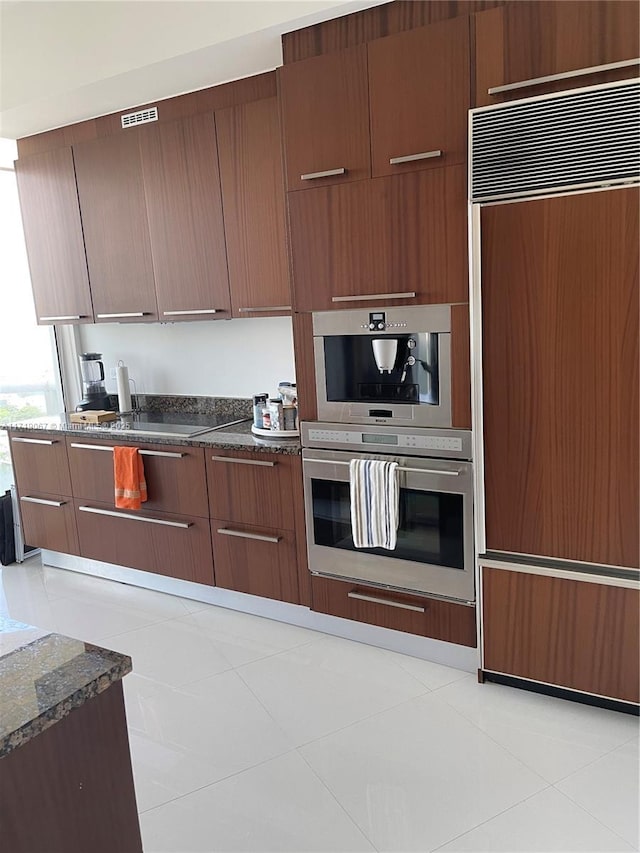 kitchen with paneled built in fridge, light tile patterned floors, and dark stone counters