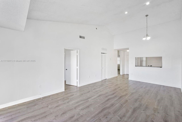 unfurnished living room featuring a textured ceiling, high vaulted ceiling, and light hardwood / wood-style flooring