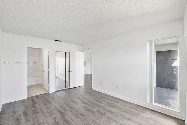 unfurnished bedroom featuring ensuite bath, light hardwood / wood-style floors, and a textured ceiling