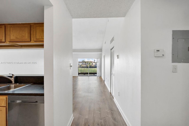 hallway with electric panel, sink, light hardwood / wood-style floors, and a textured ceiling