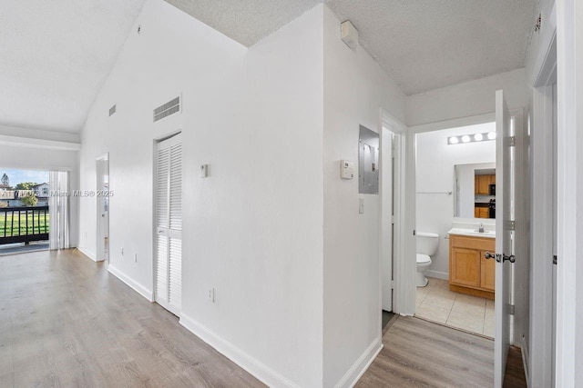 corridor with lofted ceiling, sink, a textured ceiling, and light wood-type flooring