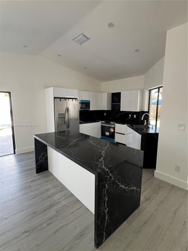 kitchen with white cabinetry, a large island, stainless steel appliances, dark stone countertops, and vaulted ceiling