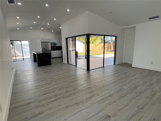 unfurnished living room with high vaulted ceiling, light wood-type flooring, and a wealth of natural light