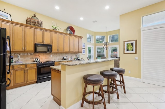 kitchen with light stone countertops, tasteful backsplash, black appliances, a center island with sink, and hanging light fixtures