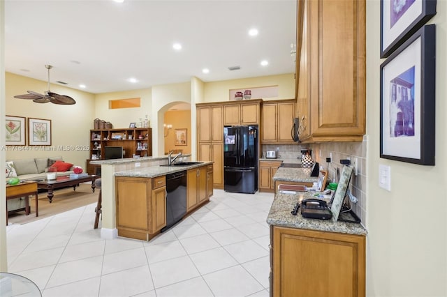 kitchen with tasteful backsplash, light stone counters, a kitchen island with sink, sink, and black appliances