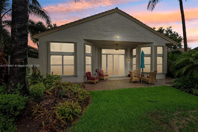 back house at dusk with ceiling fan, a yard, and a patio