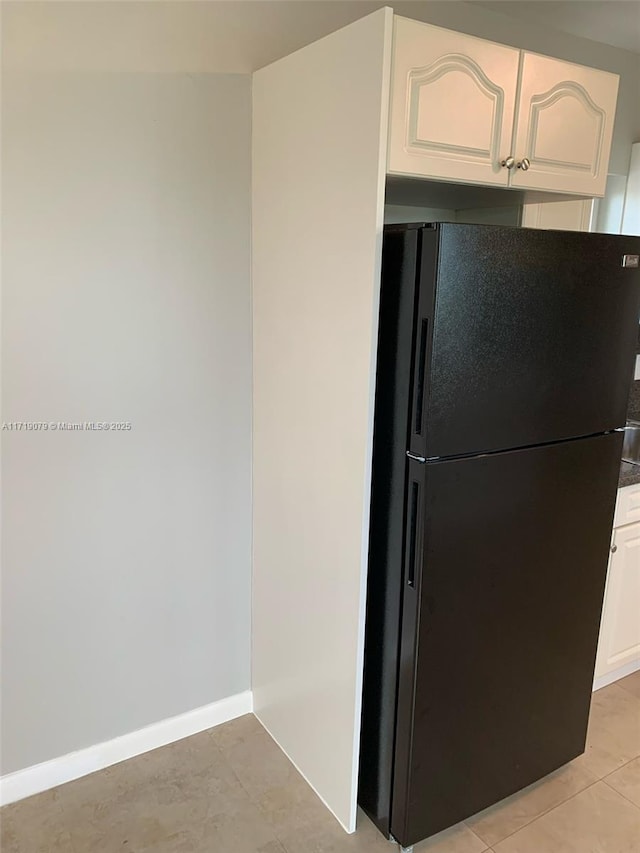 kitchen featuring black refrigerator, light tile patterned flooring, and white cabinetry