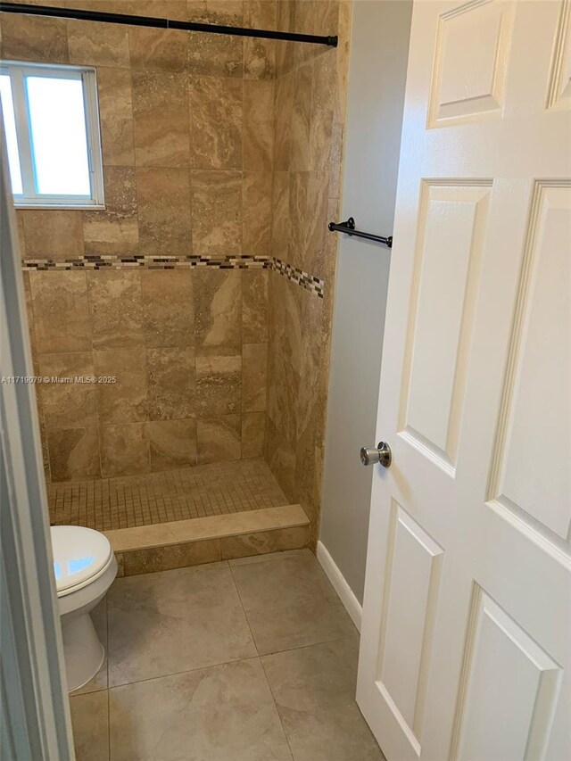 bathroom with tile patterned flooring, toilet, and a tile shower